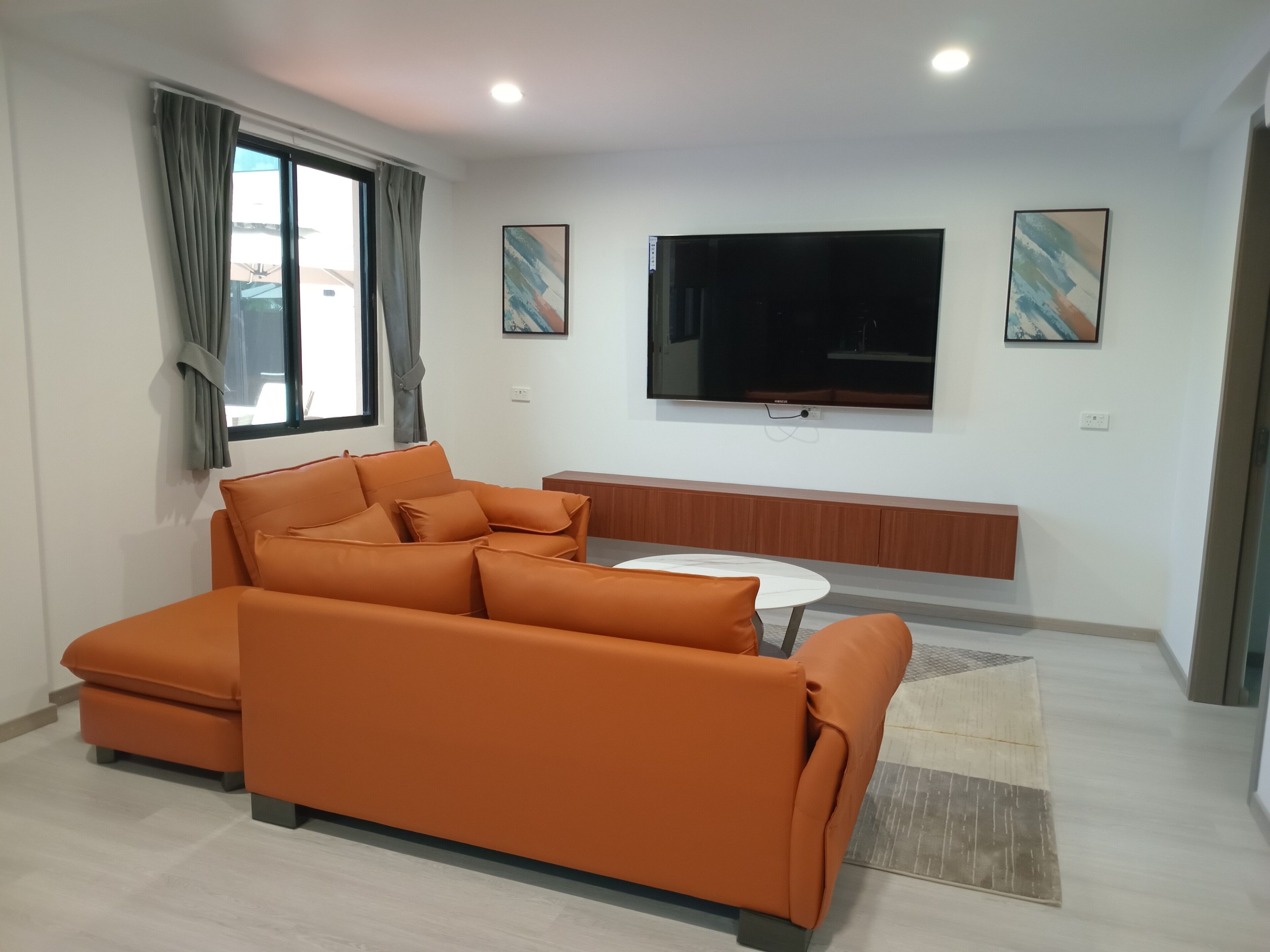Een moderne woonkamer met een hoekbank, een aan de muur bevestigde televisie en een klein rond tafeltje.