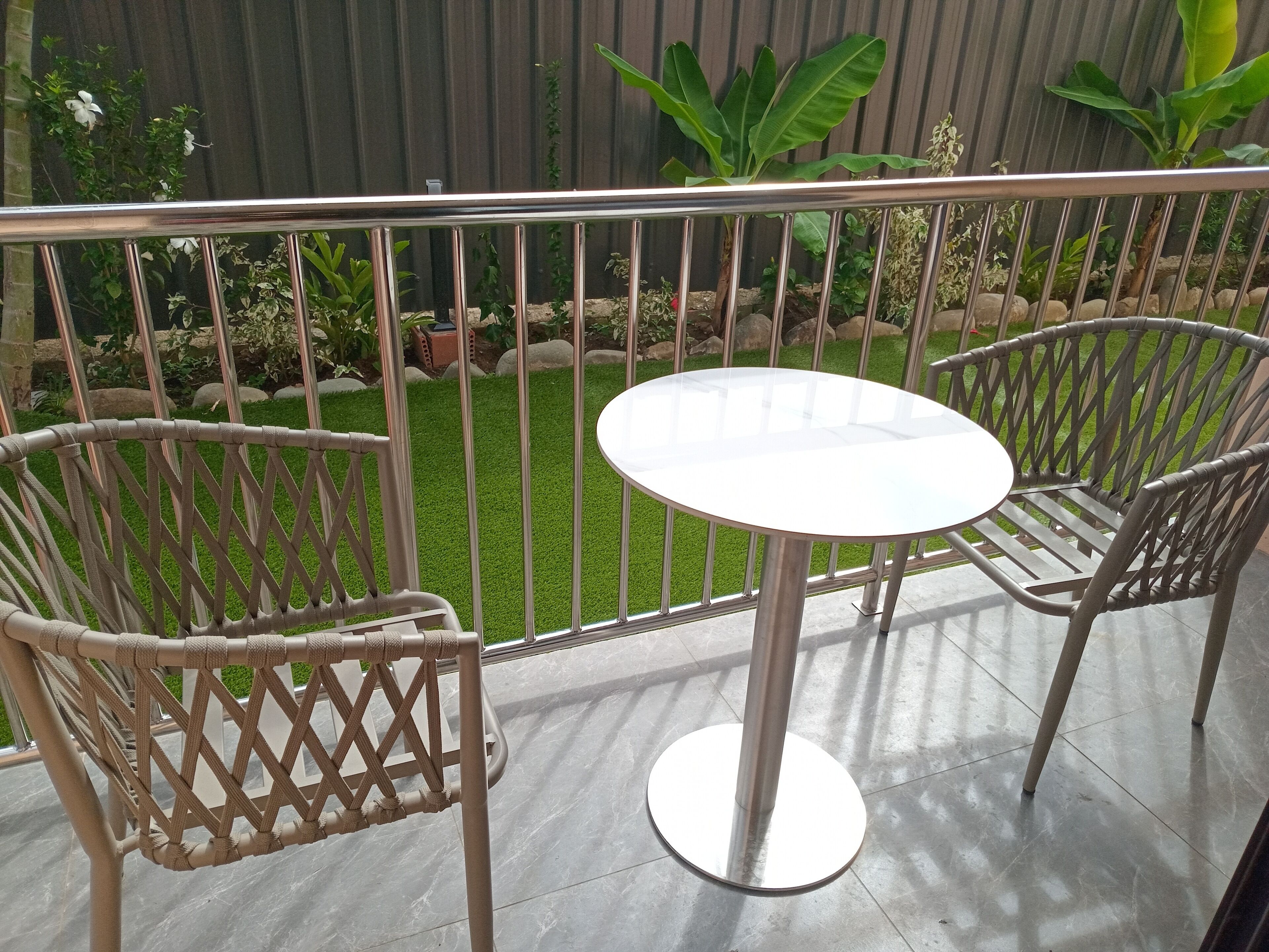 A balcony with a round table and two wicker chairs, surrounded by a metal railing.