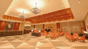 A spacious lobby with a geometric patterned floor, a reception area with a marble counter, and multiple seating areas with orange chairs. - Sotogrande Hotel and Convention Center Batangas (Bauan)
