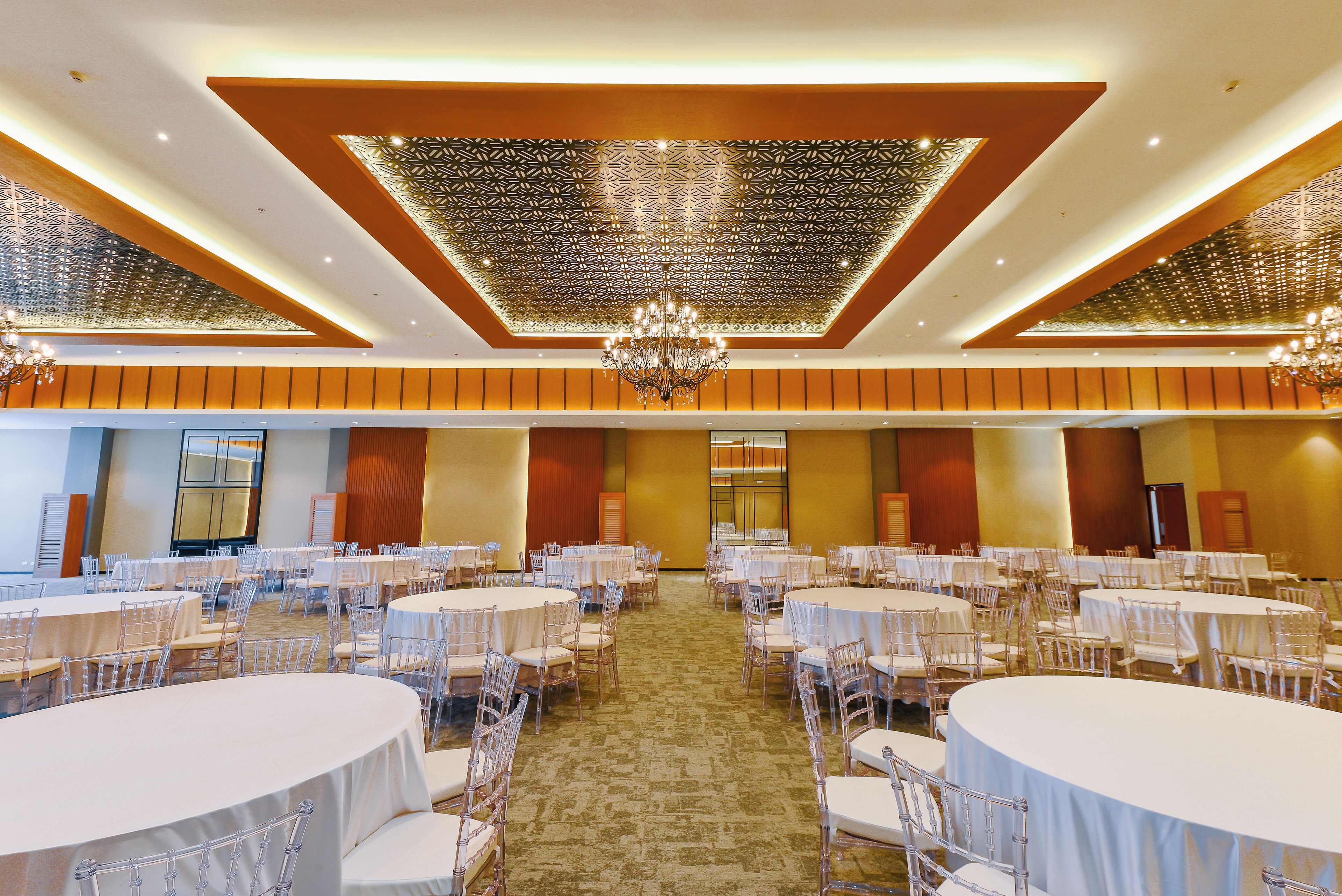 A banquet hall with round tables and chairs, a patterned ceiling, and chandeliers.