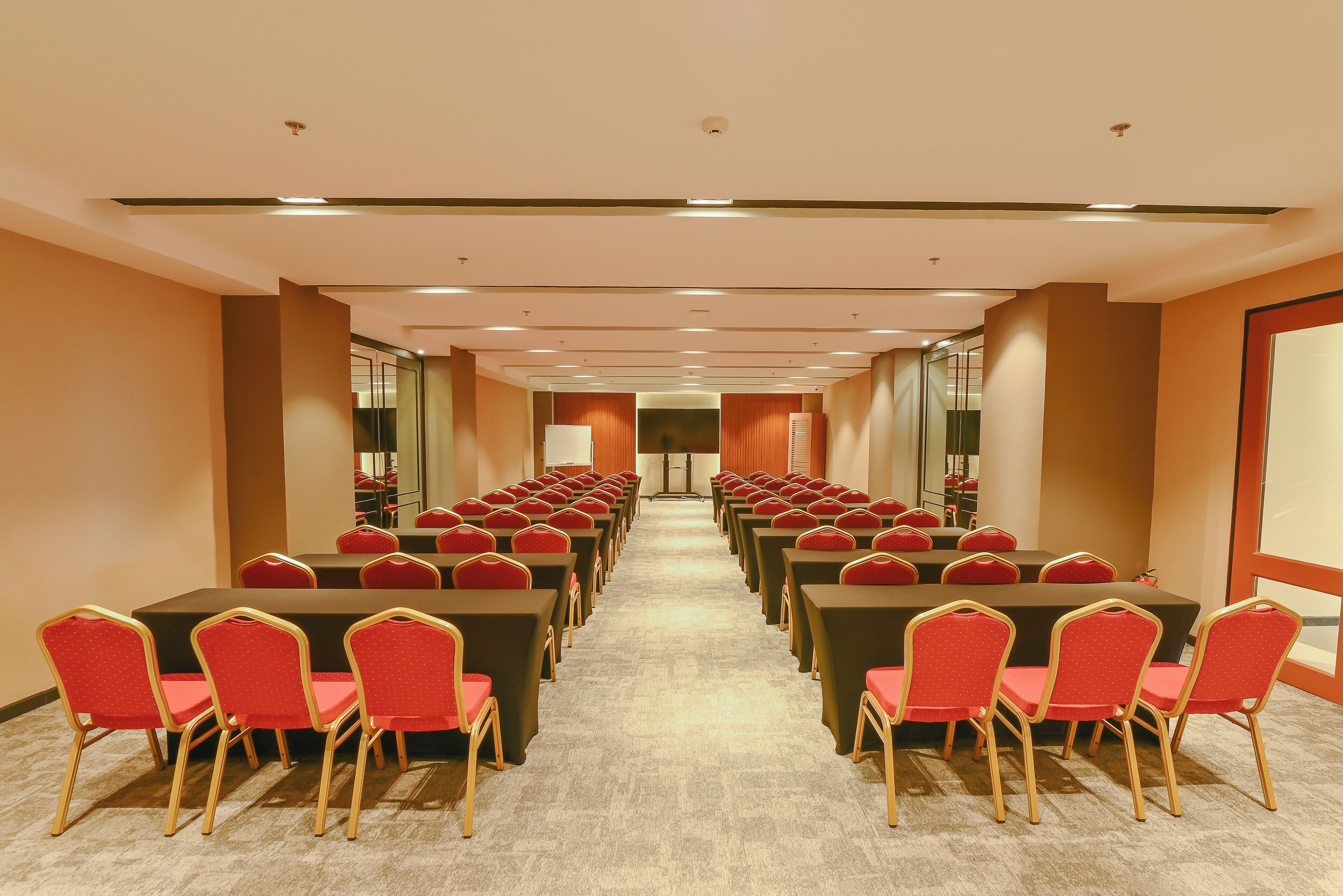 A conference room with rows of tables and chairs, a carpeted floor, and a ceiling with recessed lighting.