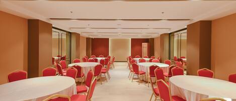 Une salle de conférence avec plusieurs tables rondes et des chaises rouges, disposées en rangées.