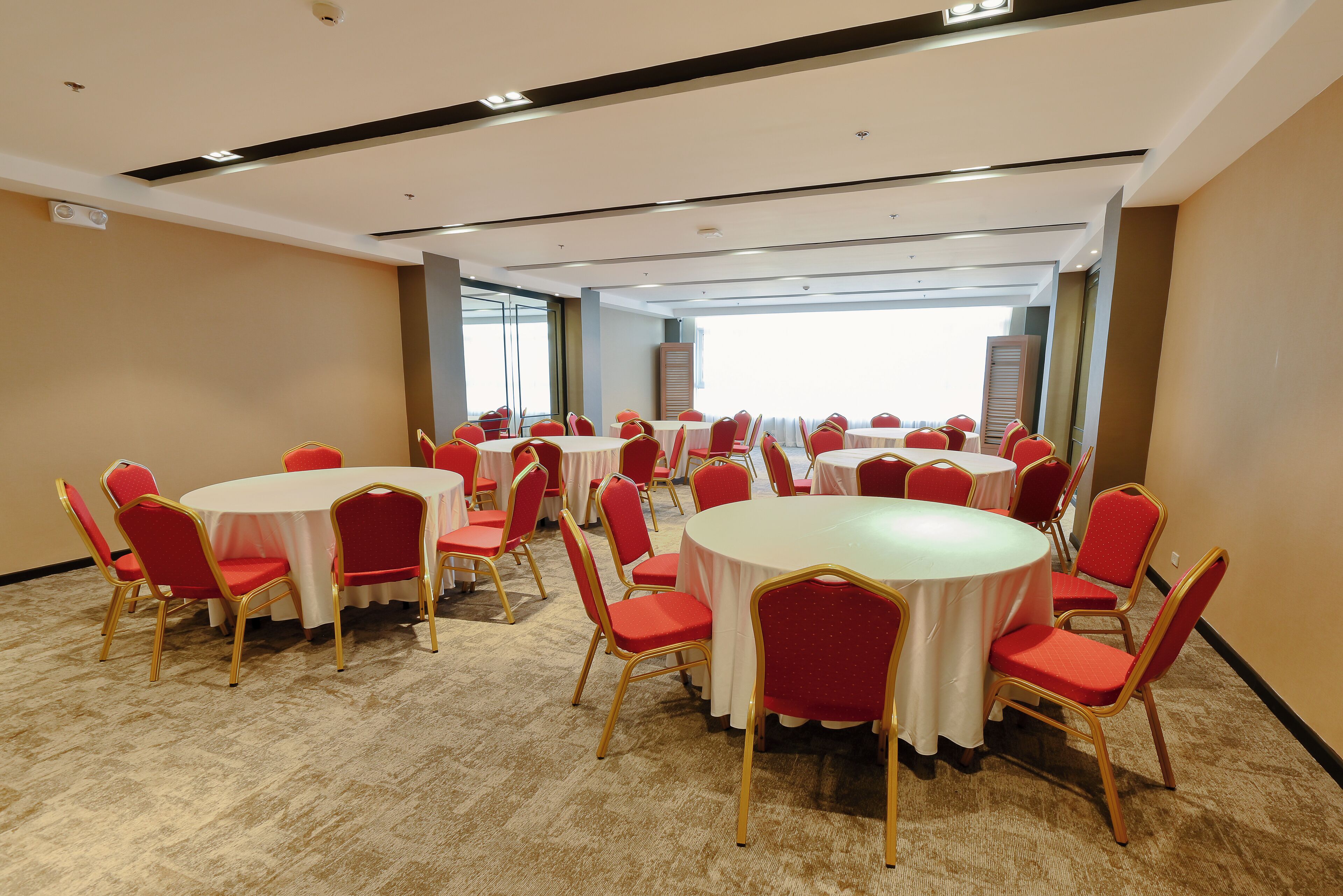 A conference room with multiple round tables and red chairs, carpeted floor, and large windows.