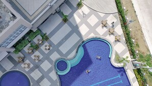 An aerial view of a swimming pool area with two pools, surrounding seating, and a landscaped garden. - Sotogrande Hotel and Convention Center Batangas (Bauan)