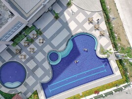 Vista aérea de una zona de piscina con dos piscinas, asientos alrededor y un jardín ajardinado.