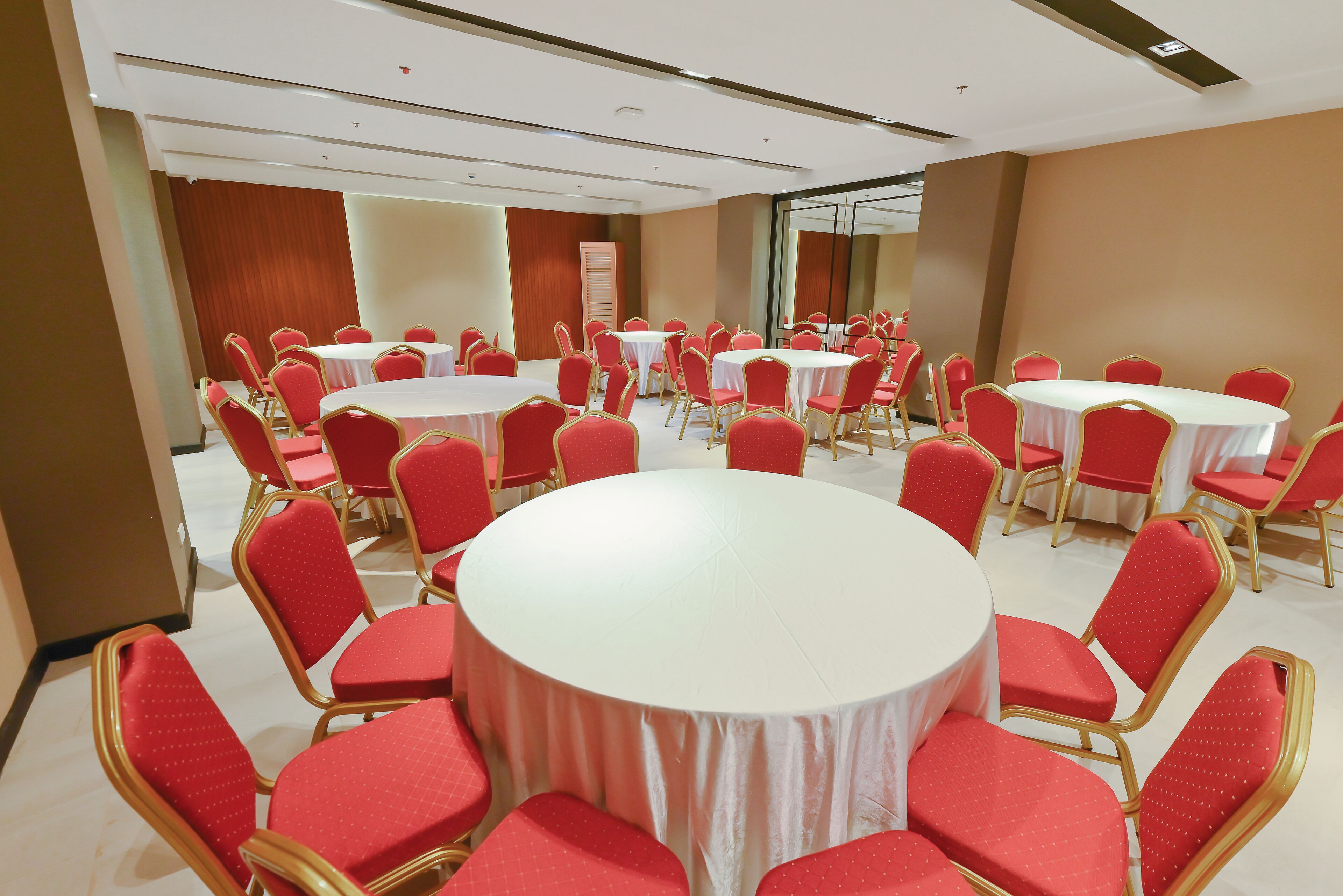 Een congrescentrum met meerdere ronde tafels en rode stoelen, gerangschikt in een U-vorm.