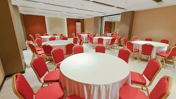Une salle de conférence dotée de plusieurs tables rondes et de chaises rouges, disposées en forme de U.