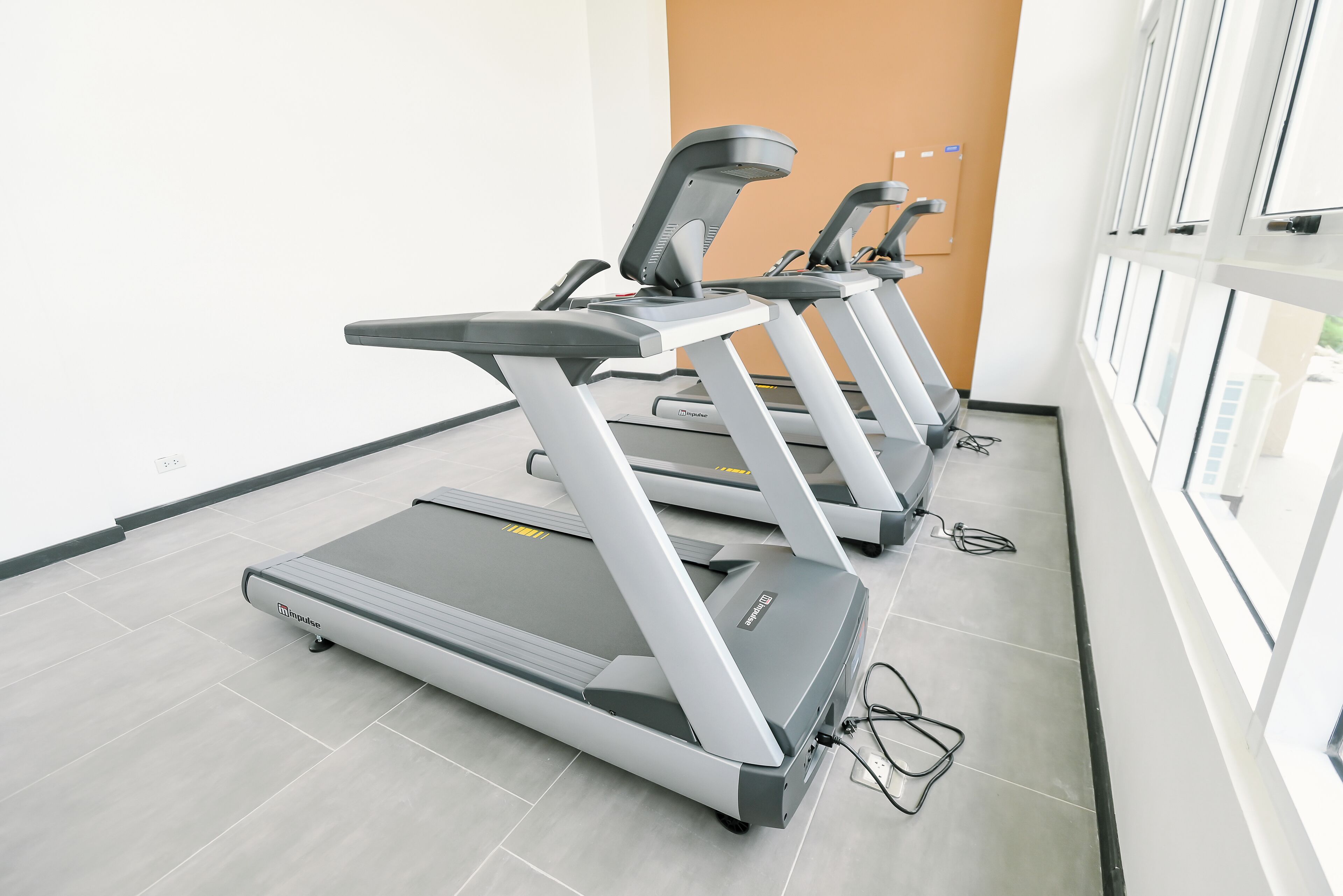 Three treadmills in a gym with a tiled floor and large windows.