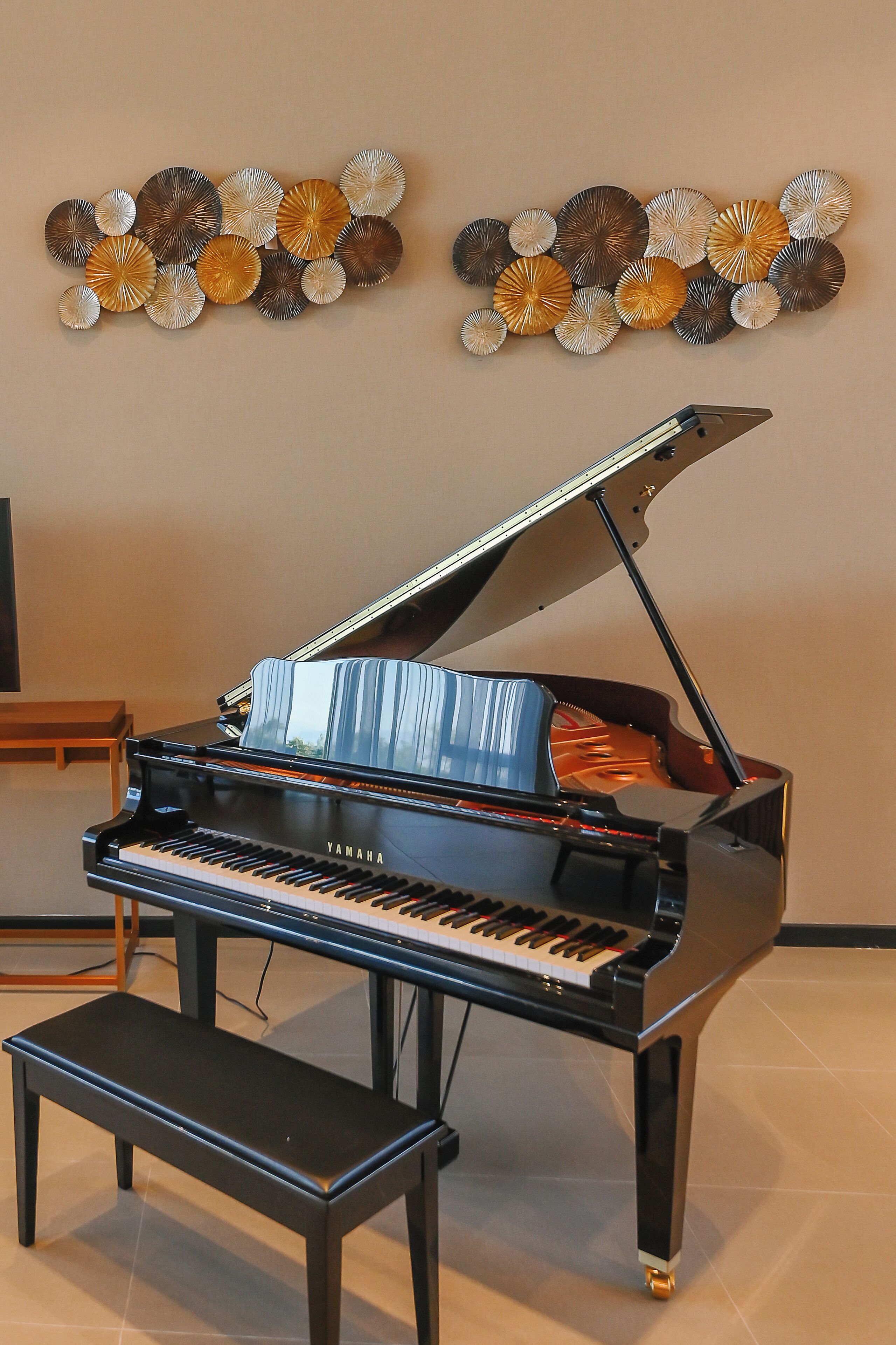 Un piano de cola con un banco en una habitación con paredes beige y detalles decorativos en las paredes.