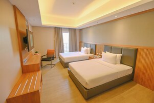 Habitación de hotel con dos camas, un escritorio, una silla, un televisor y una ventana con cortinas.