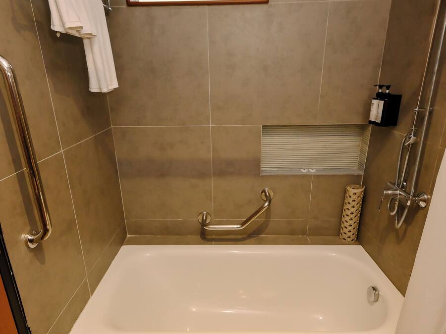 A bathroom with a bathtub, a shower, and a handrail.