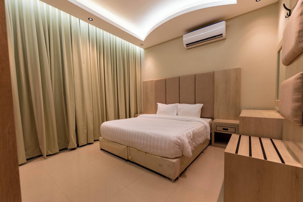 Une chambre d’hôtel moderne avec un grand lit, une table de chevet, une petite table et un climatiseur fixé au mur.
