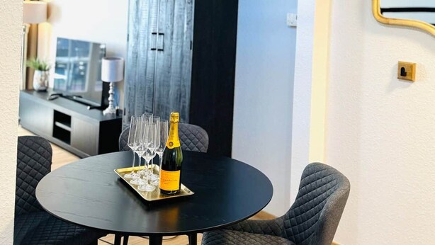 Ein runder Esstisch mit einer Champagnerflasche und Gläsern, umgeben von gepolsterten Stühlen.
