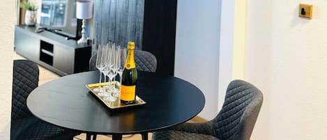A round dining table with a bottle of champagne and glasses, surrounded by upholstered chairs.