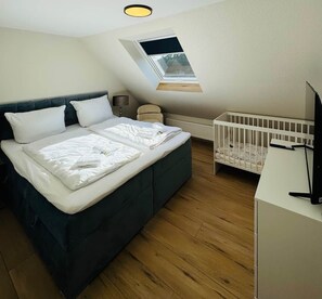 A bedroom with a bed, a crib, a desk, and a skylight. - Antonia Vacation Home (Varel)