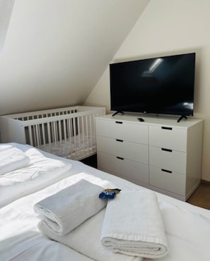 A hotel room with a crib, a television on a dresser, and neatly folded towels on the bed. - Antonia Vacation Home (Varel)