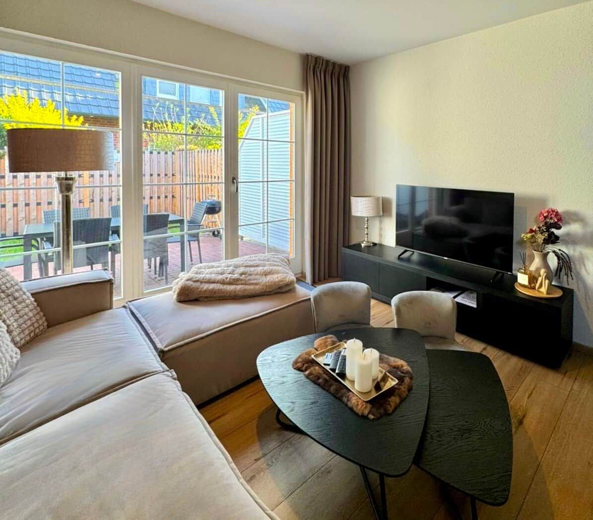 A modern living room with a sofa, a coffee table, a TV, and a view of the outdoors.