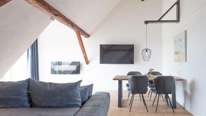 Un salon moderne avec un canapé gris, une table à manger en bois et des chaises, un téléviseur à écran plat et des œuvres d’art accrochées aux murs.
