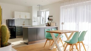 A modern kitchen with white cabinets, a black refrigerator, and a wooden dining table with green chairs.