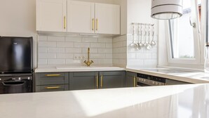 A modern kitchen with white cabinets, a black refrigerator, and a stainless steel range hood.