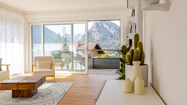A modern living room with a wooden coffee table, a beige armchair, and a large window offering a mountain view.