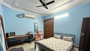 A bedroom with a bed, a desk, a chair, a wardrobe, a ceiling fan, and an air conditioner. - Nivas In Lucknow (Lucknow)