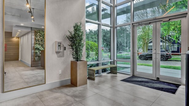 A modern lobby with large windows, a wooden bench, and a potted plant. - Luxury 1260sq ft 2 Bd/2BTH in DT (Orlando)