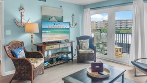 Uma sala de estar ampla com vista para a varanda, uma cadeira de madeira, um sofá e uma televisão exibindo 'Legacy Vacations'.