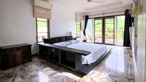 A bedroom with a large bed, a ceiling fan, and a view of greenery through the windows. - Mountain View Villa Kamala (Kamala Subdistrict, Kathu District)