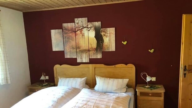 Una cama de madera con ropa de cama blanca, un cabecero de madera, dos mesitas de noche con lámparas y una pared decorada con una obra de arte de varios paneles.