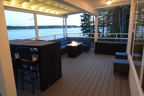 A covered outdoor deck with a seating area, a fire pit, and a view of a lake. - Modern 2-bedroom lakefront cottage (Church Point)