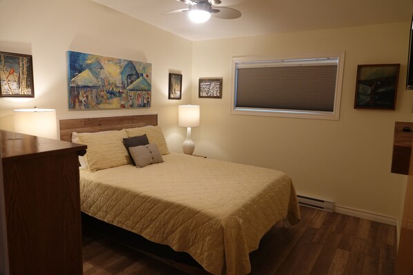 A bedroom with a bed, a ceiling fan, a window with blinds, and wall art. - Modern 2-bedroom lakefront cottage (Church Point)