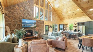 Amplia sala de estar con chimenea de piedra, asientos cómodos, cocina equipada con electrodomésticos modernos y ventanas grandes que ofrecen vistas.
