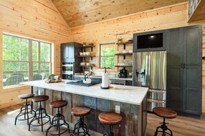 A wooden cabin kitchen with a large island, bar stools, stainless steel appliances, and a TV mounted above the island. - Soaring National Park Views/Pool (Gatlinburg)