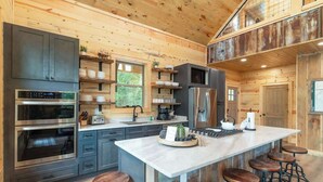Una cocina moderna con una isla central, taburetes de bar y un nivel entre pisos.
