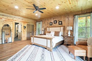 A wooden cabin bedroom with a bed, a ceiling fan, a nightstand, a chair, and a window.