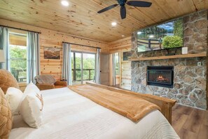A bedroom with a large bed, a stone fireplace, and a view of a lake. - Soaring National Park Views/Pool (Gatlinburg)