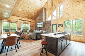 A spacious kitchen with a large island, wooden walls, and large windows offering views of the outdoors. - Soaring National Park Views/Pool (Gatlinburg)