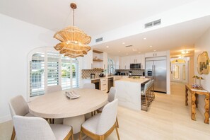 A modern kitchen with white cabinetry, a central island, and a dining area with a round table and chairs.