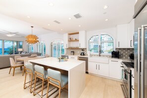 A modern kitchen with white cabinets, a central island with bar stools, a large window, and a view of the ocean.