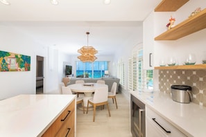 A modern kitchen with white cabinetry, a dining area with a round table and chairs, and a view of the ocean through large windows.