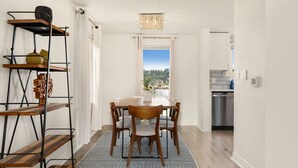 A dining area with a round table, six chairs, a patterned rug, and a metal shelving unit with decorative items.