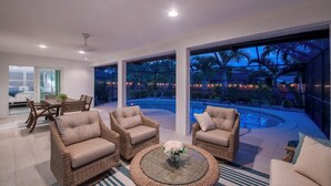 A modern outdoor living area with wicker furniture, a glass coffee table, and a view of a swimming pool at dusk. - Pet-Friendly 3-Bedroom Home with Pool (Bonita Springs)