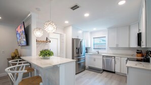 A modern kitchen with white cabinetry, stainless steel appliances, and a central island with bar stools. - Pet-Friendly 3-Bedroom Home with Pool (Bonita Springs)