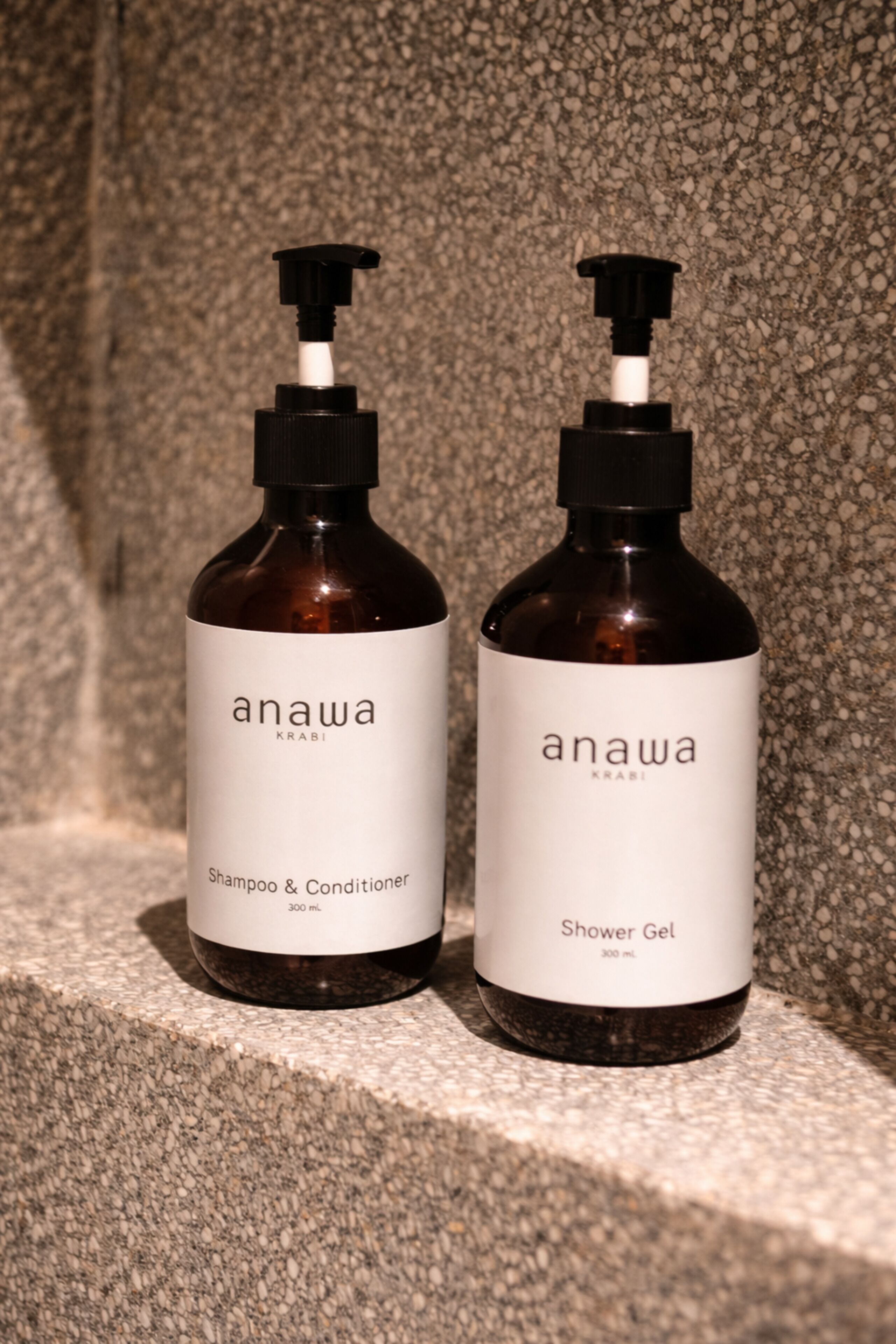 Zwei Flaschen Anawa Shampoo, Conditioner und Duschgel auf einer strukturierten Oberfläche.