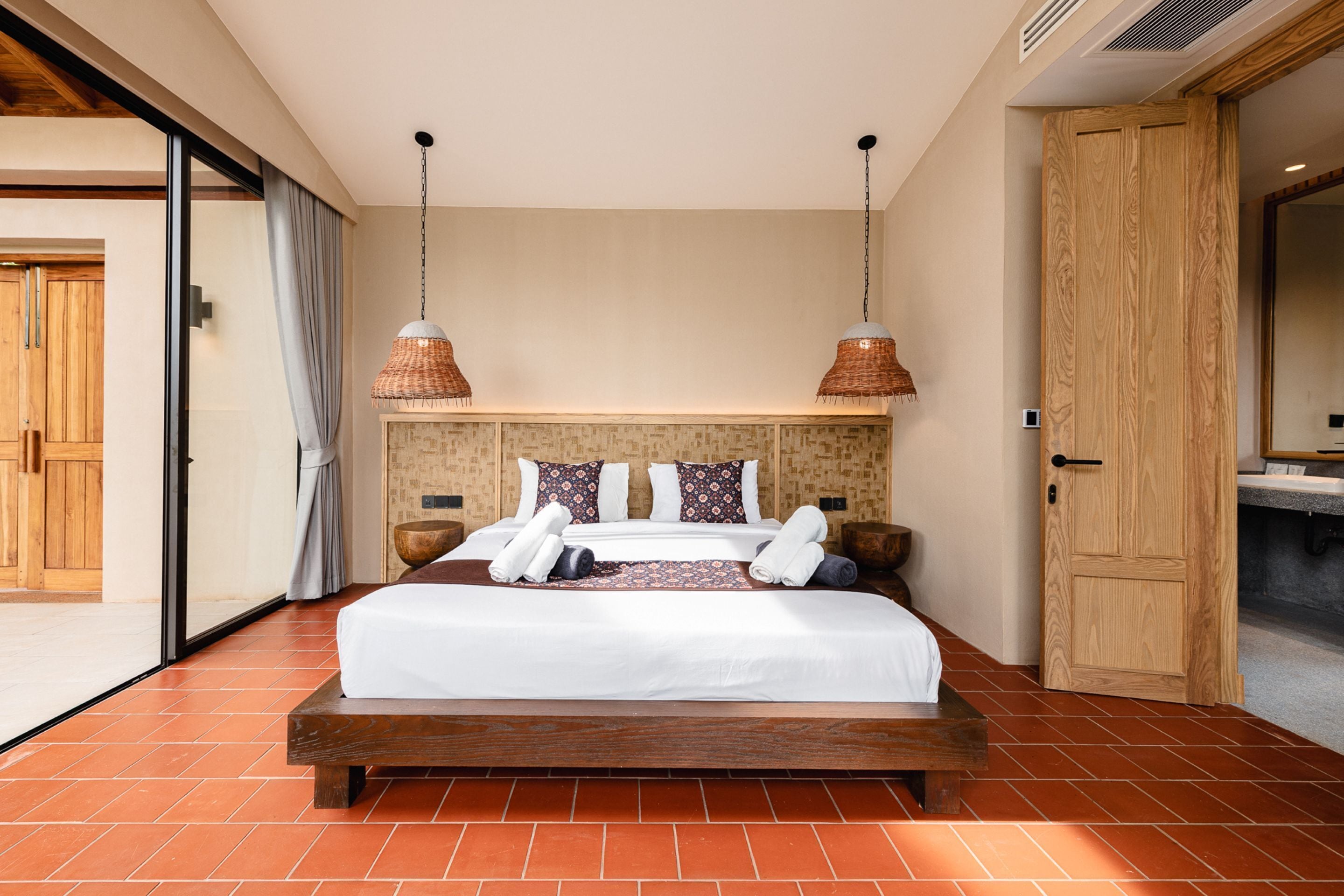 A spacious bedroom with a large bed, two bedside tables, a wooden wardrobe, and a sliding glass door leading to a balcony.