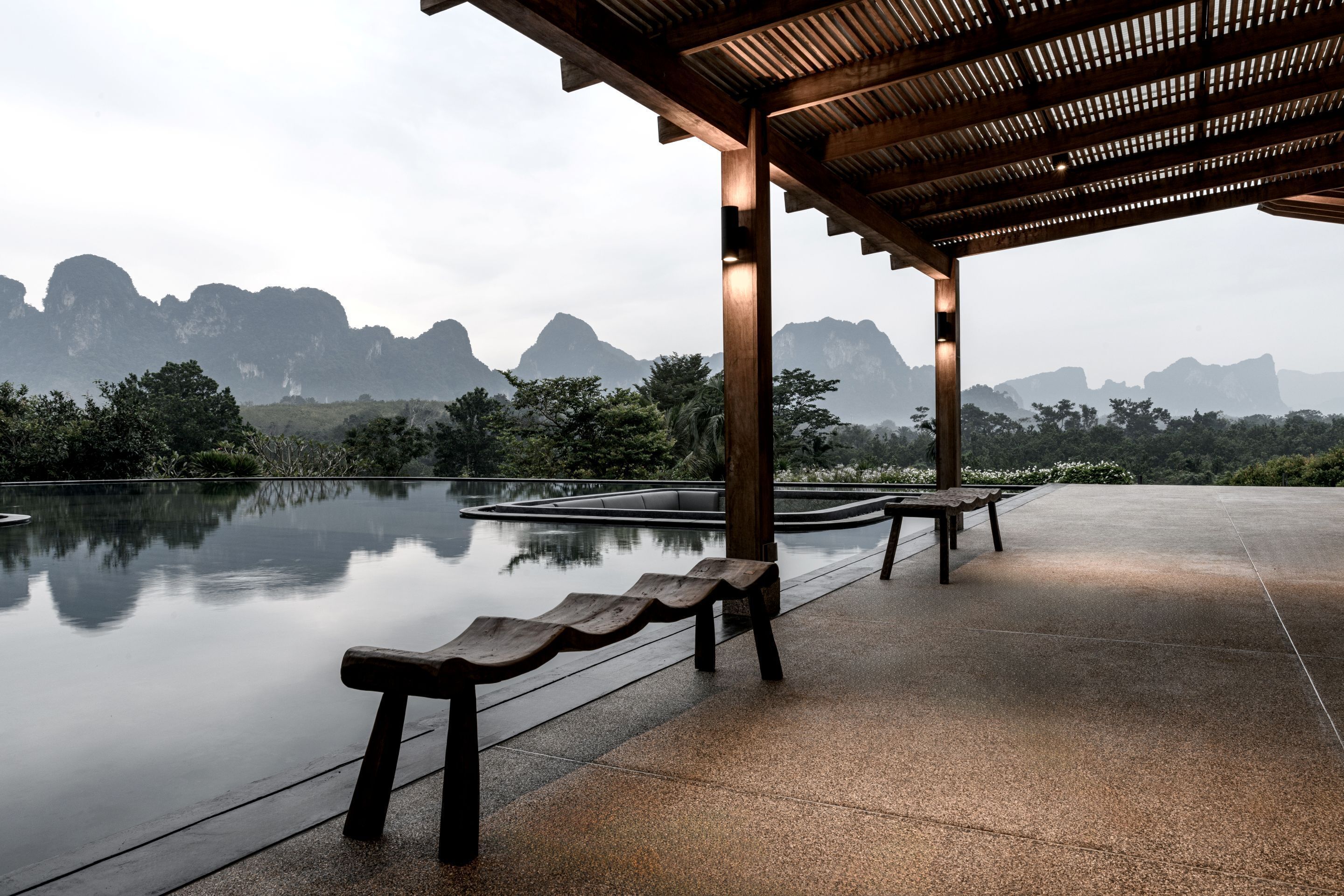 A tranquil outdoor seating area with wooden benches and a reflective pool, overlooking a mountainous landscape.