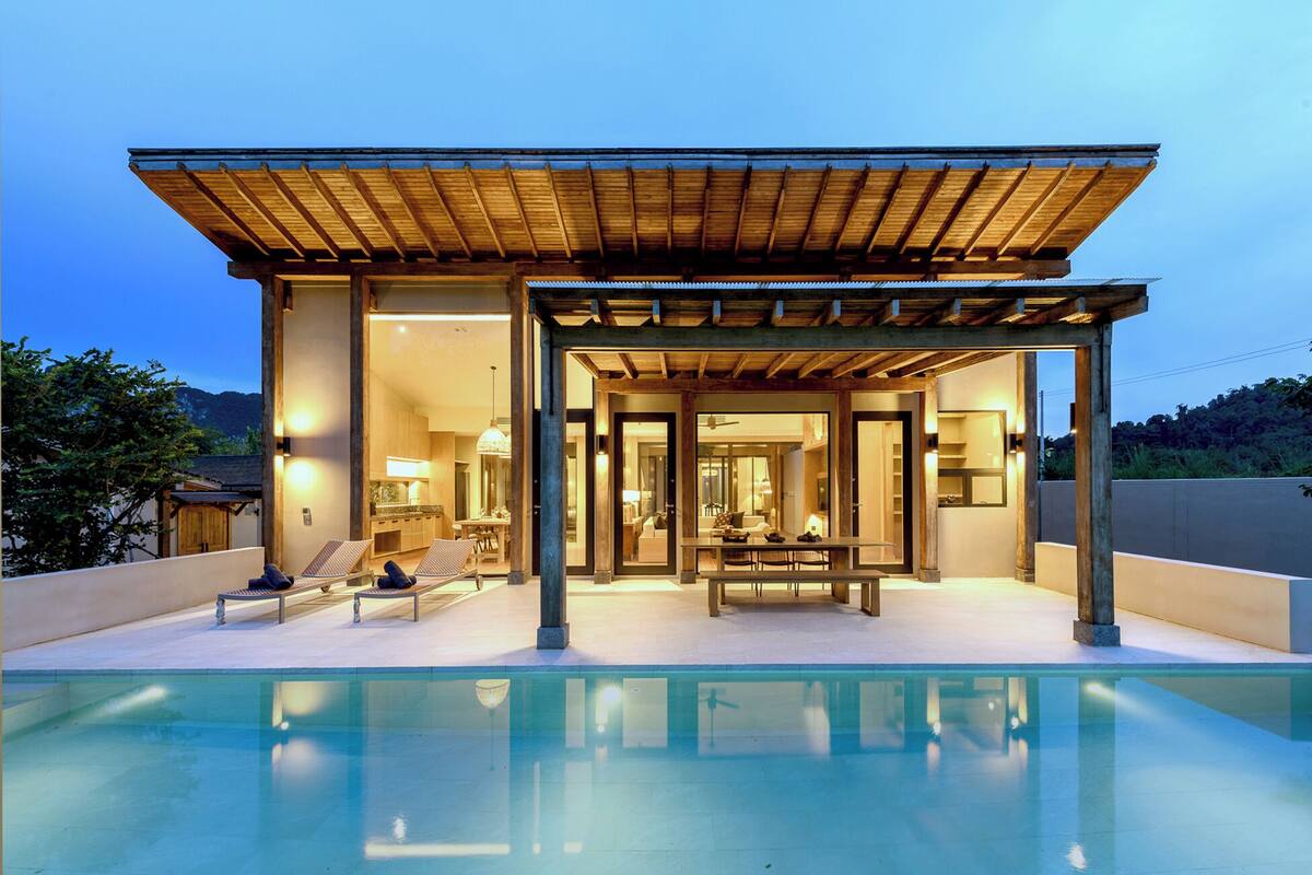 Una casa moderna con piscina, que presenta un patio cubierto con zona de estar y mesa de comedor.