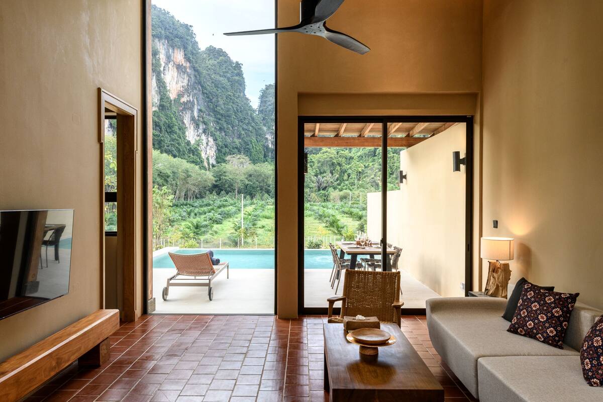 Amplia sala de estar con televisor grande, asientos cómodos y vistas a la montaña y la piscina.