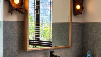 A bathroom with a large mirror, wooden wall decor, a white sink, and a bottle of hand soap.